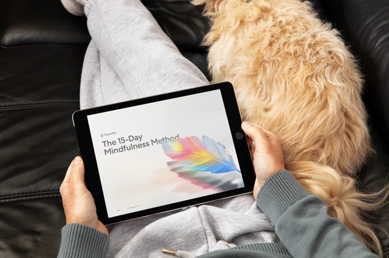 A person sits on a couch holding an iPad with The 15-Day Mindfulness Method journal by Paperlike open on the screen.