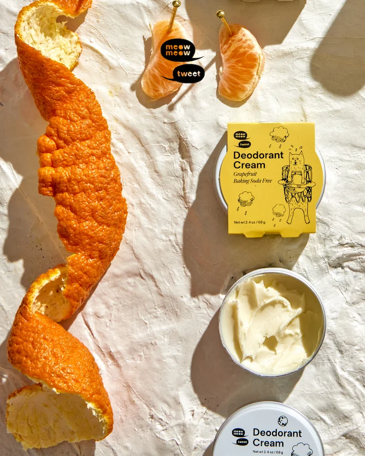 Three tins of deodorant cream are set on a plaster background with slices citrus and rind.