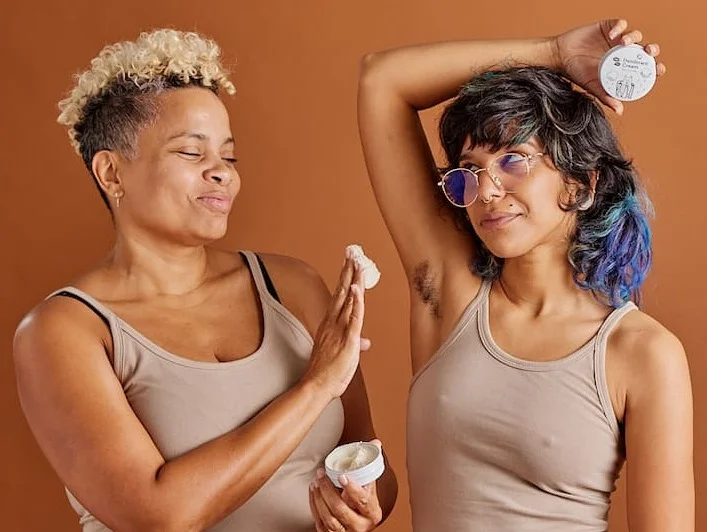 A person has a big scoop of deodorant cream they are going to apply to another persons armpit.