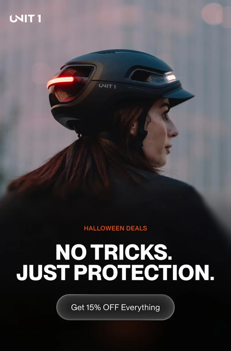 Woman riding at dusk wearing UNIT 1 smart helmet with rear lights on. Headline: No tricks. Just protection.