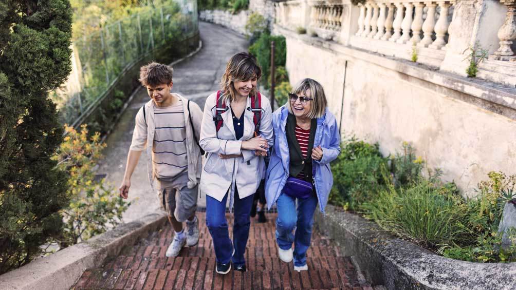 Image description: Senior woman, her mature daughter and teenage grandson walking up stairs.
