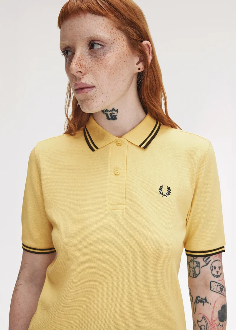White female model wears a G3600 Champions Gold Fred Perry Shirt