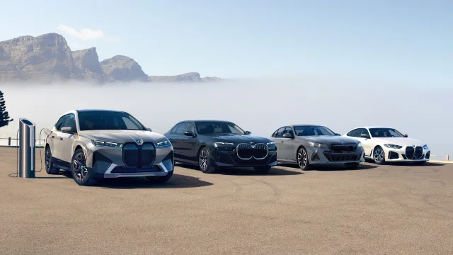 BMW iX, i7, i5, i4 parked in front of mountains.
