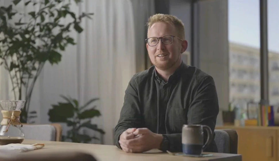 A picture of a person sitting at a desk with their hands together