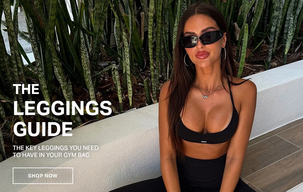 Woman in black sports bra and leggings, sitting outdoors amongst green plants, wearing sunglasses. Promotes "The Leggings Guide" for gym bag essentials.