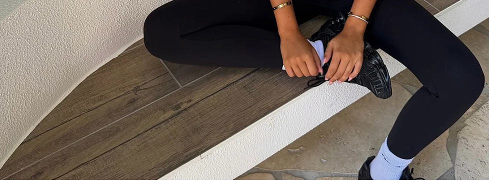 Seated person in black leggings and sneakers, hands adjusting laces. Showcases comfortable, stylish athletic wear perfect for everyday fitness.