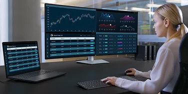 An office worker tracking the status of recent orders across multiple dashboards on a widescreen Dell UltraSharp 52 TBT monitor, laptop, wireless keyboard and mouse.