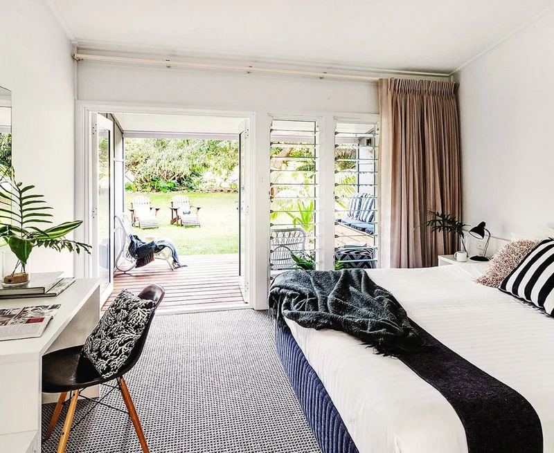 Image description: A bright and airy hotel room with a view of a deck that opens to a grassy backyard.