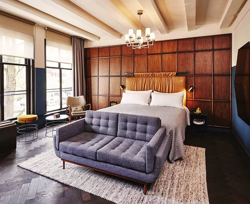 Image Description: A white bed with a brown leather headboard behind a blue velvet couch.