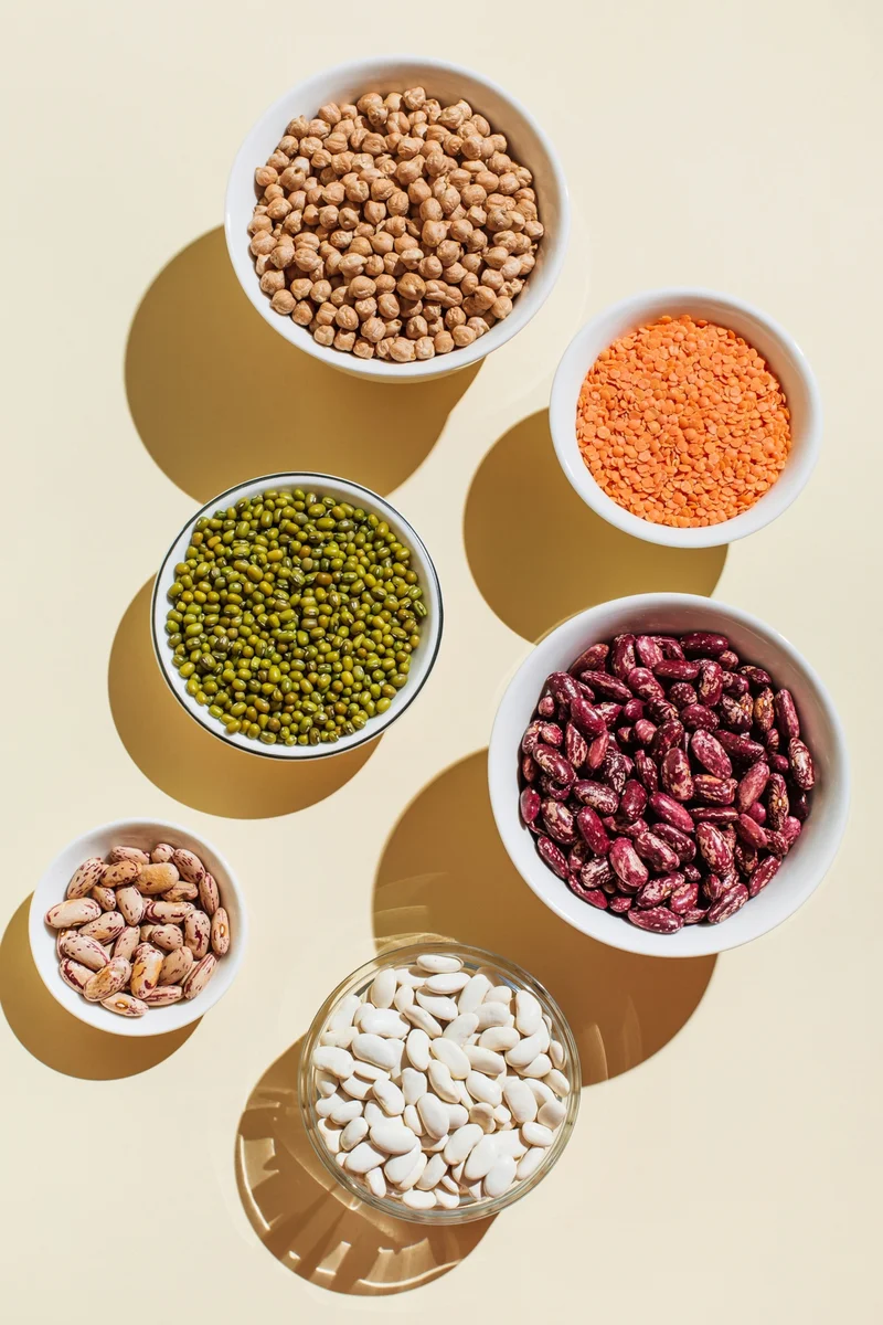 Overhead shot of several bowls containing different foods high in fiber like nuts, chickpeas, lentils and red beans.