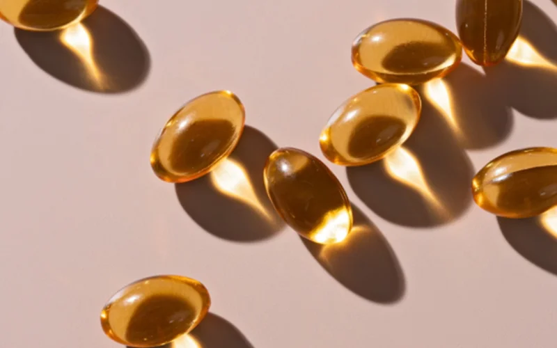 Several capsules of omega-3 (fish oil) pills are shown on a salmon pink background.