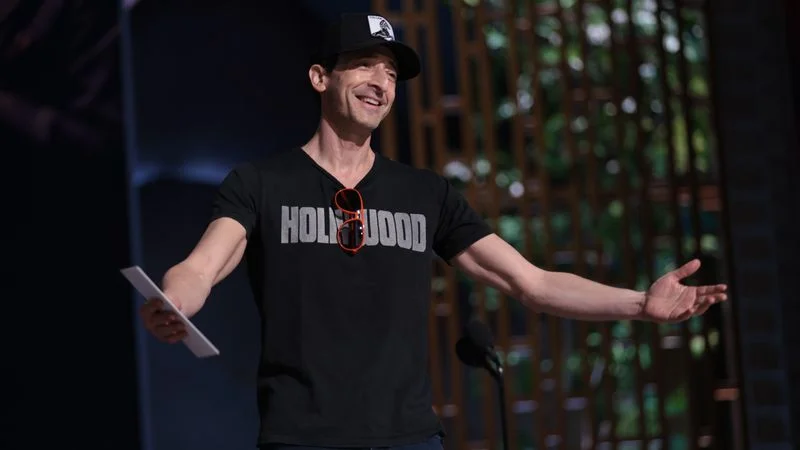 Image may contain: Adrien Brody, Clothing, T-Shirt, Performer, Person, Solo Performance, People, Baseball Cap, Cap, and Hat