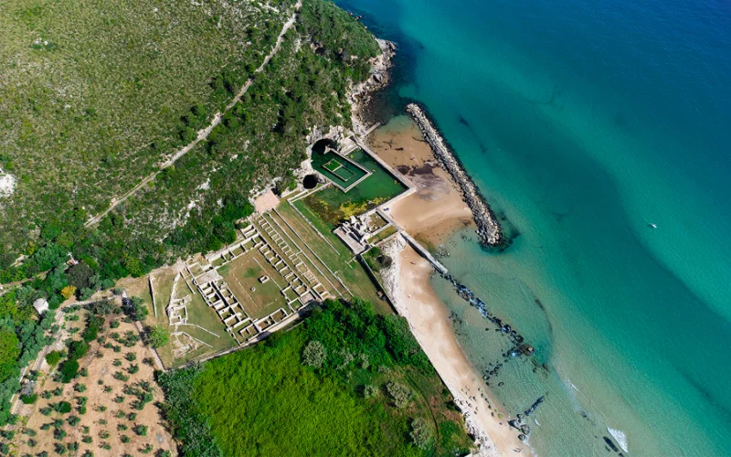 An aerial view of the Sperlonga site shows the ruins of Tiberius’s villa, the grotto mouth, and the pool cut into the beach.