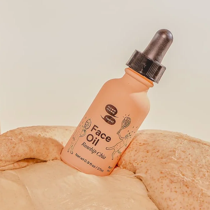 A pink bottle of face oil is balancing atop a dough like substance.