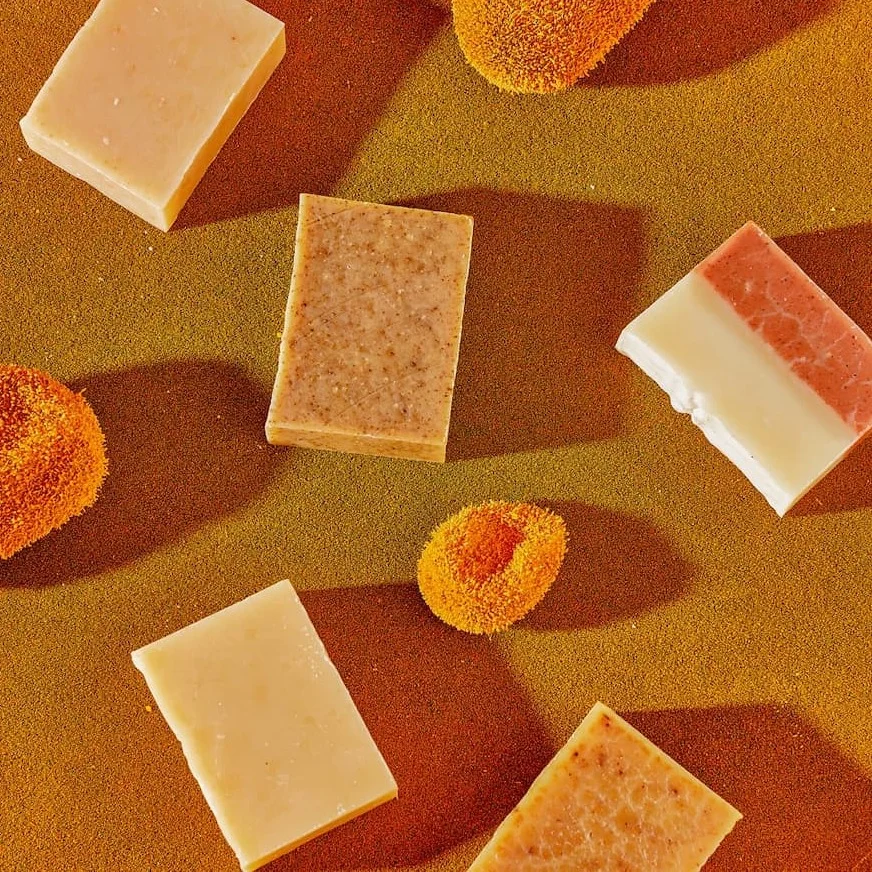 Five bars of soap are strewn against a brown backdrop with sea sponges in between.