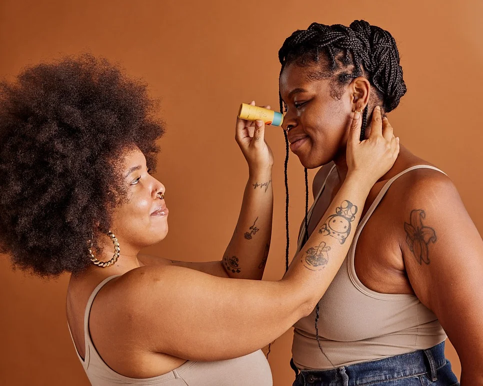 A person applies a stick of repair balm to another persons nose.