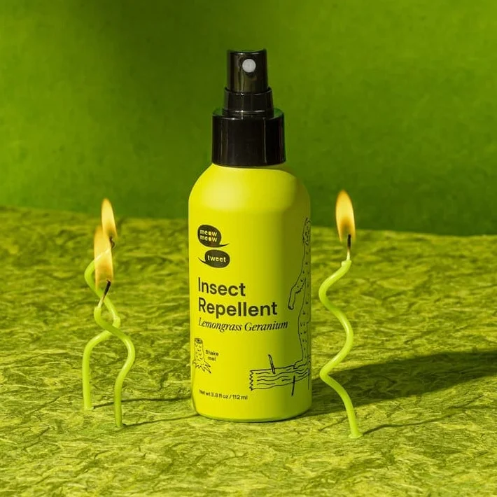 A green bottle of insect repellent stands on a green backdrop with green birthday candles burning around it.