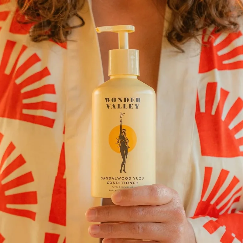 A person wearing a bathrobe is holding up a yellow pump bottle of conditioner.