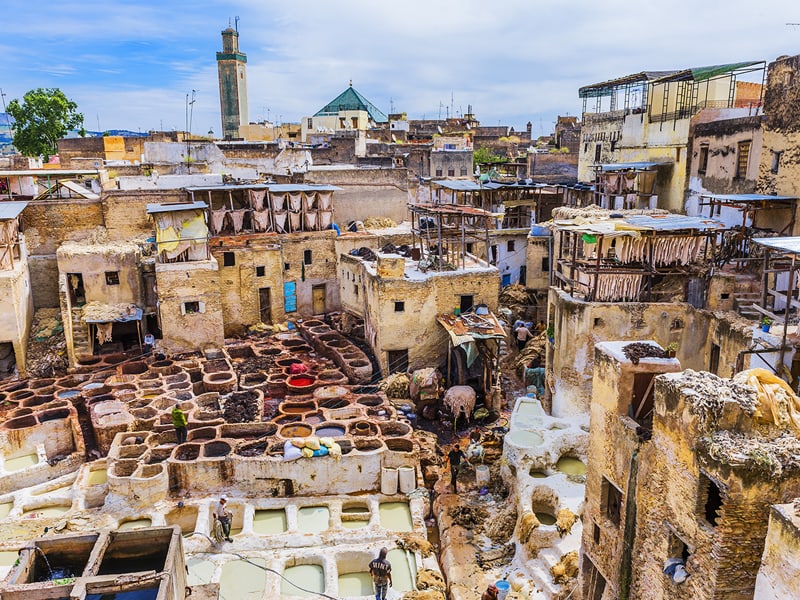 A view of Chouwara Tannery in Fes el Bali (Old Fes), Medina, showcasing traditional leather tanning processes with colorful dye pits and bustling activity.