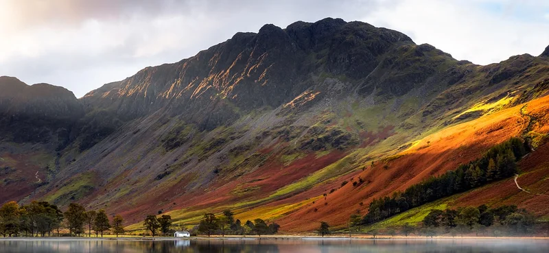 Haystacks mountain reflected in the calm waters of Buttermere, surrounded by vibrant autumn foliage in the Lake District, Cumbria, England.