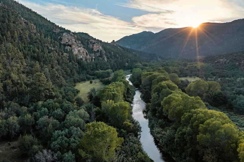 Aerial image of lush mountains with river running through the middle during sunset.