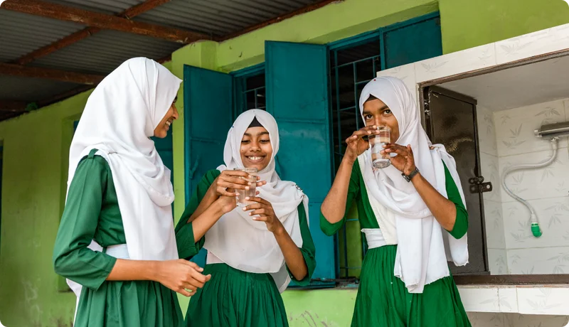 Three young girls in school uniforms drink clean water.