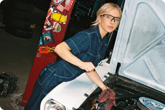 Sydney Sweeney reaching under the hood of a blue 1964½ Ford Mustang® convertible