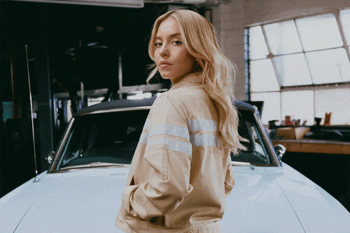 Sydney Sweeney standing in front of a blue 1964½ Ford Mustang® convertible with Ford x Sydney Sweeney in text