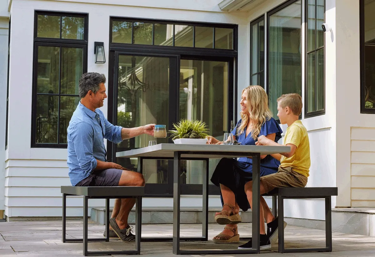 Family outside with an Arlo Essential Outdoor Camera mounted on the house.