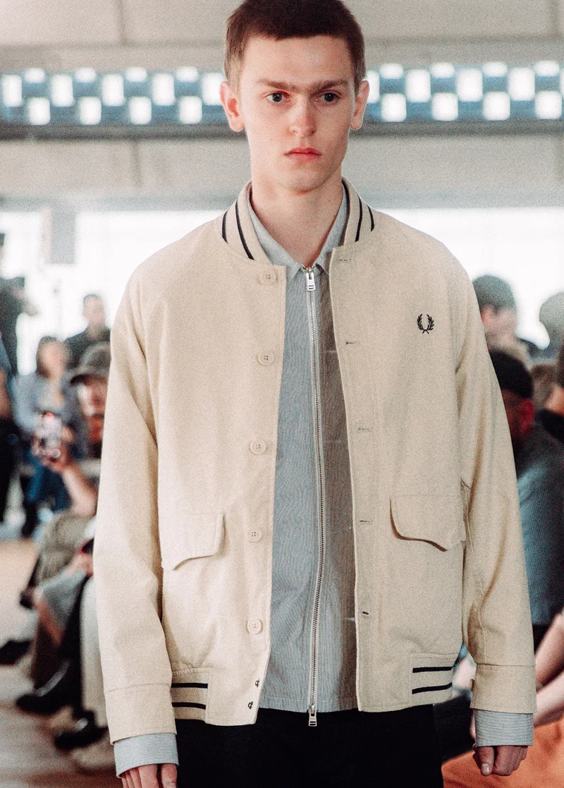 White male model with short light brown hair walks our runway wearing our new beige tennis bomber jacket