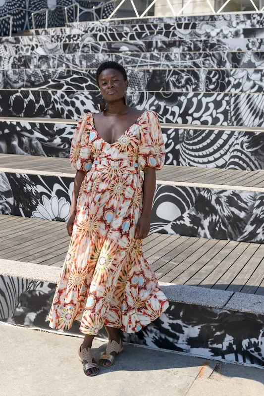 A woman stands in front of an art installation on the front steps of the Brooklyn Museum