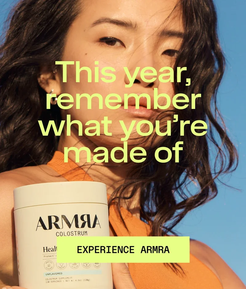 Woman holding a jar of ARMRA Colostrum against a blue sky, representing strength, vitality, and natural beauty.