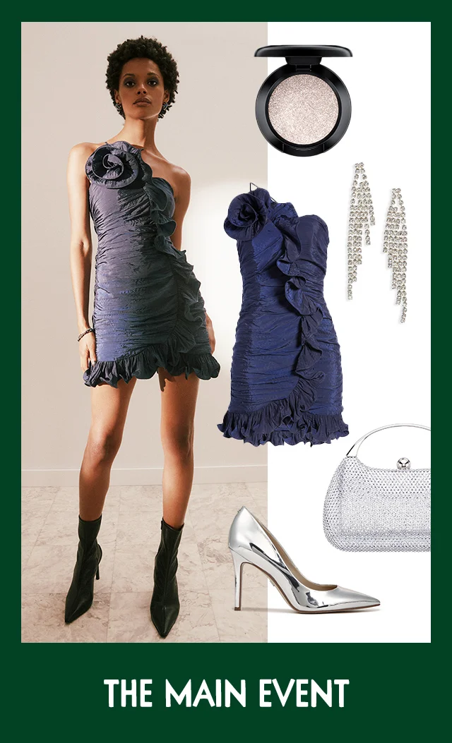A woman wearing a navy minidress with a rosette detail. A silver clutch, crystal fringe earrings, a silver pump and shimmery eyeshadow.