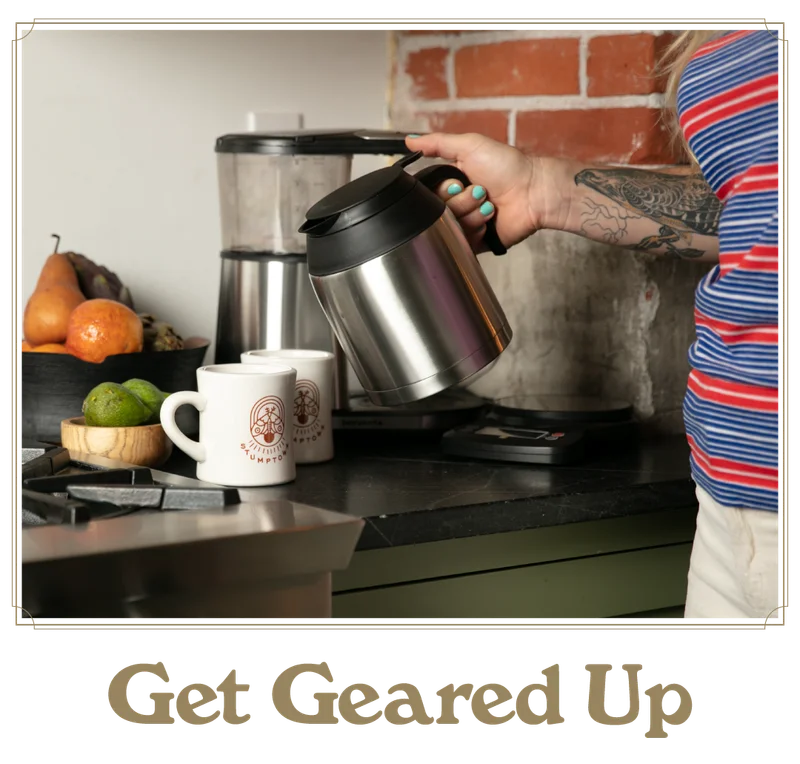 Stainless steel coffee carafe held next to a home brewer with mugs on the counter. Text reads “Get Geared Up.”