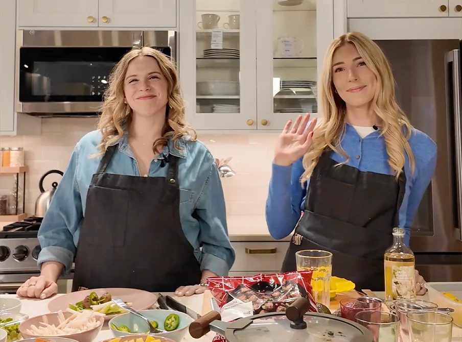 Two smiling women in aprons behind a counter.