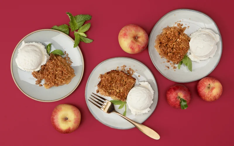 Overhead shot of three plates of apple crumble and vanilla ice cream with apples on the side.