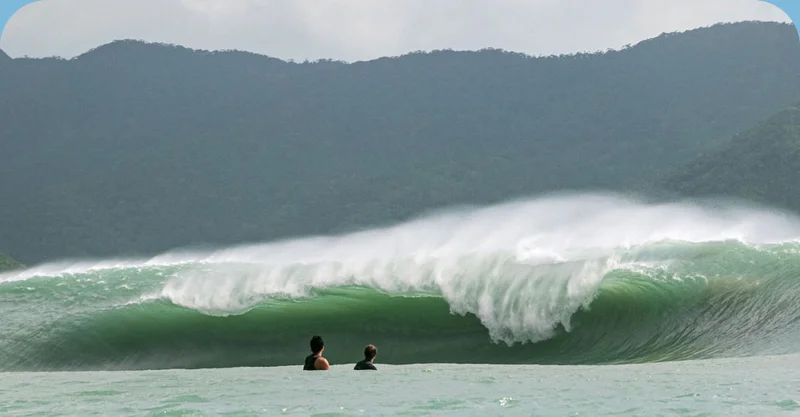 Two surfers watch a huge, extremely thick wave break from the channel.