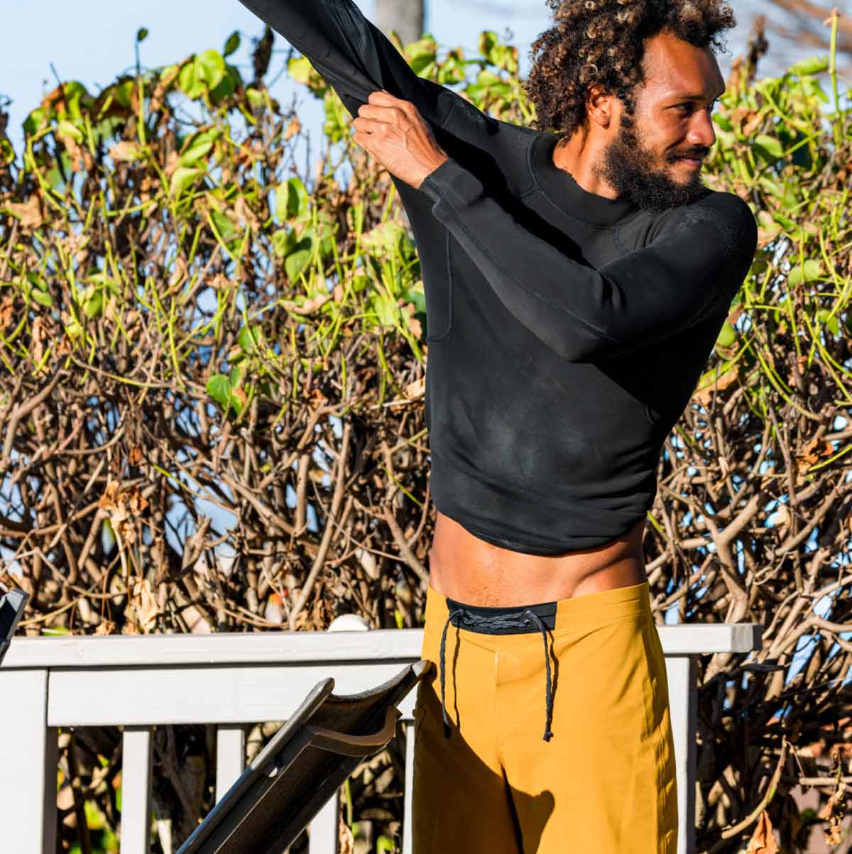 A surfer wearing Hydrolock Boardshorts puts on a wetsuit top before paddling out.