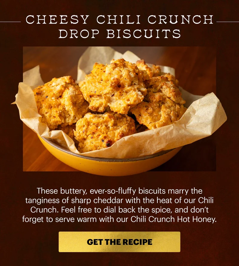 Header: CHEESY CHILI CRUNCH DROP BISCUITS. These buttery, ever-so-fluffy biscuits marry the tanginess of sharp cheddar with the hear of our Chili Crunch. Feel free to dial back the spice, and don't forget to serve warm with our Chili Crunch Hot Honey. CTA: GET THE RECIPE