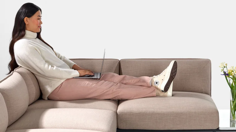 Person on laptop sat with legs stretched out on Pink Mimo Modular Seating L shape.