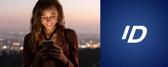 A woman smiles at her smartphone with the city skyline behind her.