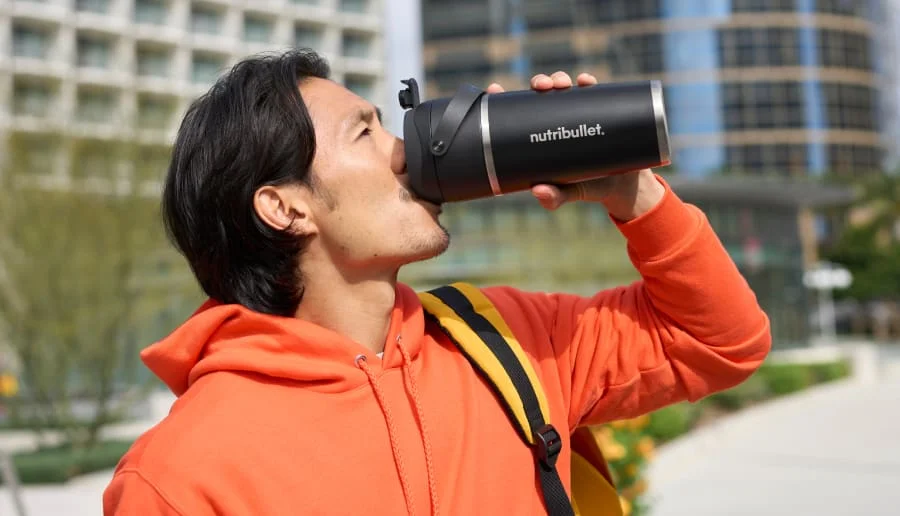 A man in an orange hoodie drinks from the nutribullet Flip outdoors, embodying an active, on-the-go lifestyle.
