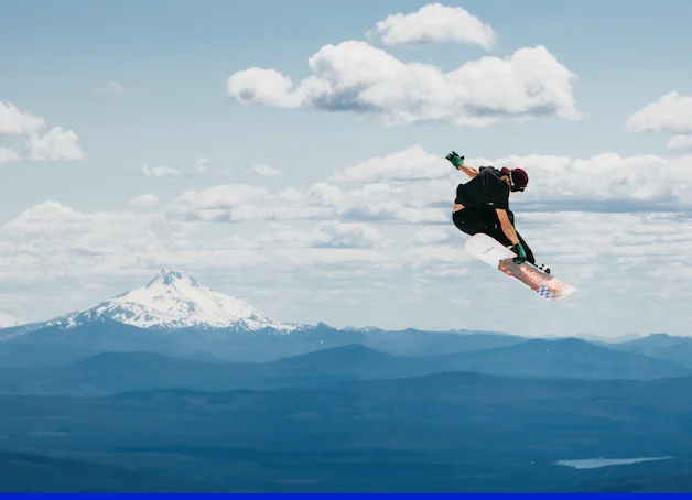 Snowboarder in the air with snowy mountains and a cloudy sky in the background