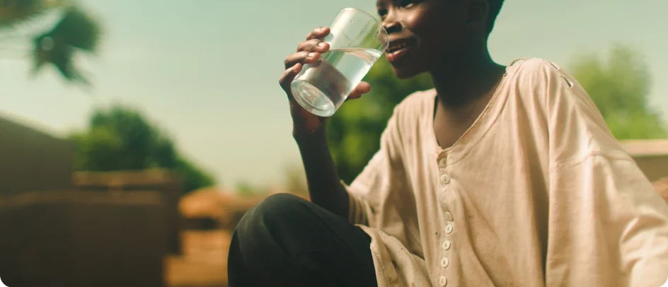 A young child drinks a glass of clean water.