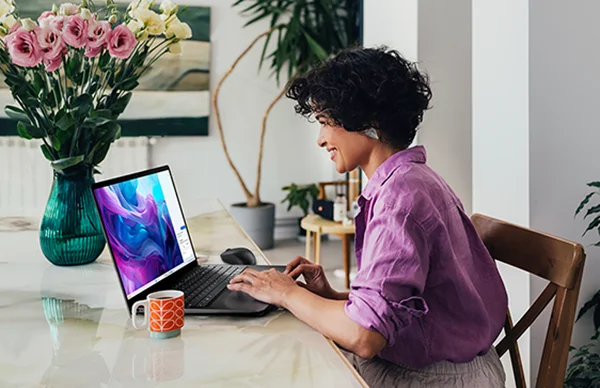 A side view of a beautiful Latin-American entrepreneur smiling while watching something on her laptop, floral arrangement on desk.