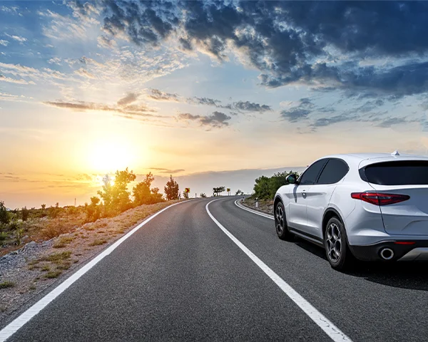 A white vehicle drives into the sunset on an open road.