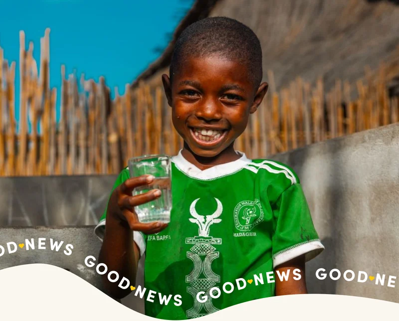 A young boy smiling with a clean glass of water in his hand.