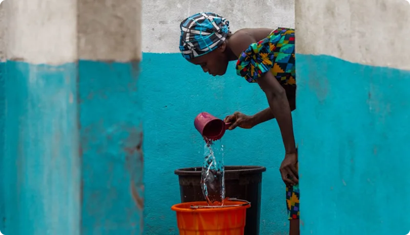 A young woman pouring water into a bucket.