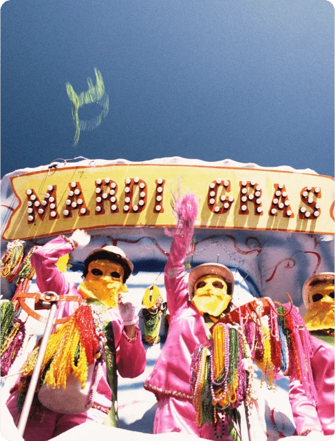 Image Description: Two colorful Mardi Gras masqueraders throwing strings of beads from a parade float