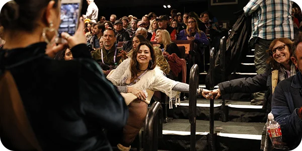 Two women sitting across an aisle holding hands and posing for a photo in a crowded theater at the
Festival.